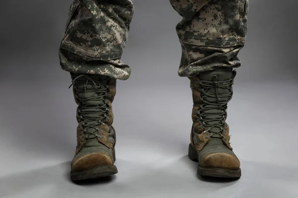 Legs of a man in a camouflage suit and army boots. Political conflicts and a turbulent military environment. Close-up. Gray background.