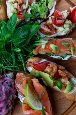 Tahta servis tahtasında kırmızı balık, limon, otlar, soğan ve sebzelerle çeşitli bruschetta. Sağlıklı ve lezzetli atıştırmalıklar. Yakın plan. Dikey.