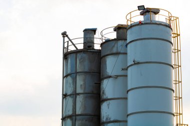 İnşaat alanı siloları. Bulutlu gökyüzü arka planında izole edilmiş depolama kuleleri. İnşaat alanının arka plan fotoğrafı. Çimento depoları.
