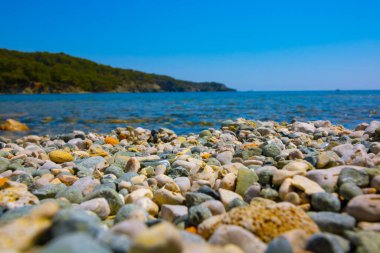 Sahilde çakıl taşları, arka planda deniz ve orman kaplı tepe olan çakıl taşları. Yaz konsepti.