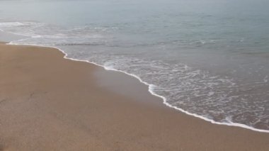Kumlu sahilde dalgalar kırılıyor. Dalgalı sakin deniz ve kumlu sahil.