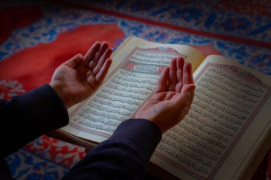 Dua eden müslüman adam. Müslüman adam arka planda el kaldırarak ve Kuran 'ı okuyarak dua ediyor. Ramazan veya kandil veya laylat al-Qadr veya İslami arkaplan fotoğrafı. Seçici odak.