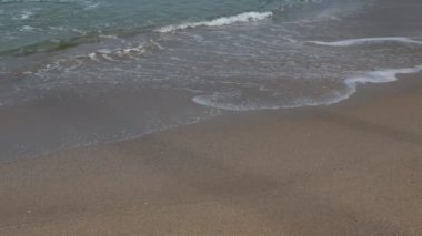 Sahilde dalgalar kopuyor. Dalgalı sakin deniz ve kumsalın alçak açısı. Yaz ya da tatil 4k arkaplan videosu.
