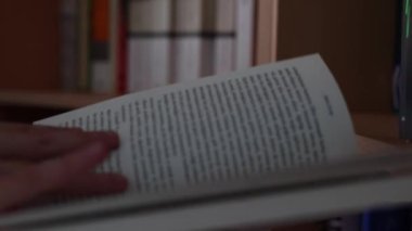 Bir kitabın sayfalarını çevirmek. Kitaplığın, kütüphanenin ya da kitapçının yakınındaki bir kitapta okuyan ya da arayan bir kadın. 4K arka plan videosu. Odaklanmamış video.