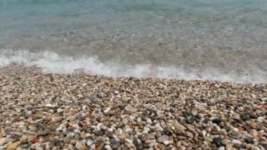 Kumsal ve dalgalar. Çakıl taşlı plaj ve dalgalı berrak deniz.