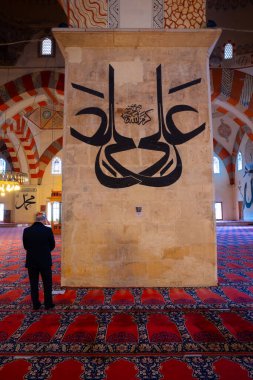 Edirne 'deki Eski Cami' nin direğinin arkasında dua eden müslüman adam. Duvarda Ali ibn Abi Talib 'in el yazısı var. Edirne Türkiye - 10.25.2021