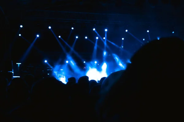 Silhouette of People in the concert area with spotlights on the stage and fog effect. Concert background photo. Noise included.