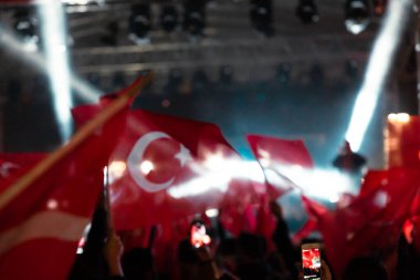Türk halkı Türkiye 'nin ulusal bayramını gece boyunca Türk bayrakları sallayarak kutluyor. Sahnedeki spot ışıkları. Bayraklarda hareket bulanıklığı.