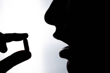 Taking pill. Silhouette of a unrecognizable woman taking a pill or drug. Healthcare or medicine or wellness or taking vitamins or recovering from illness concept photo.