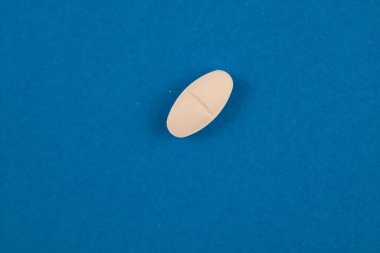 Diamond shape white pill isolated on blue background. Medicine or healthcare concept photo.
