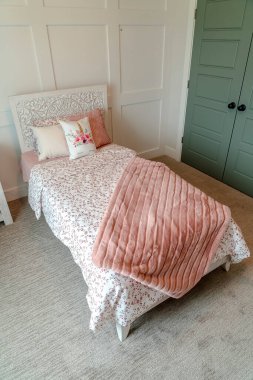Tek yataklı, kadınsı yatak odası çiçekli, küçük yastıklı ve pembe battaniyeli.