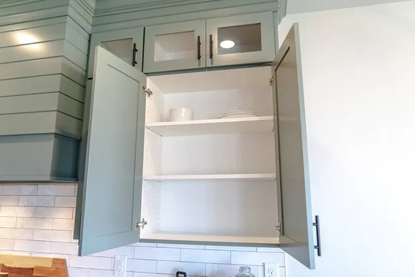 Wall cabinet with open door over white tile backsplash inside kitchen of home