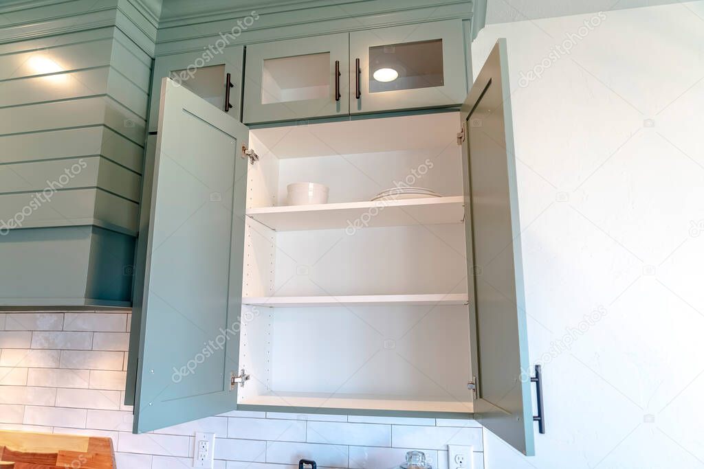 Wall cabinet with open door over white tile backsplash inside kitchen of home