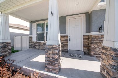 Verandasında taş kaplamalı sütun direkleri olan bir evin cephesi.