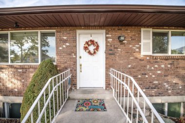 Çelengi ve renkli paspası olan bir evin beyaz ön kapısı.