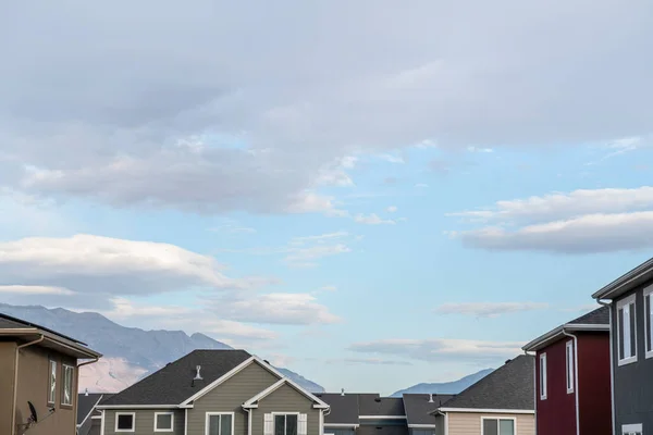 Asphalt shingle roofs of houses against the mountain and bright cloudy sky