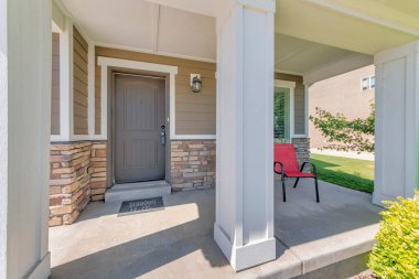 Beyaz sütun direkleri ve kırmızı kol koltuğu olan bir evin verandası.