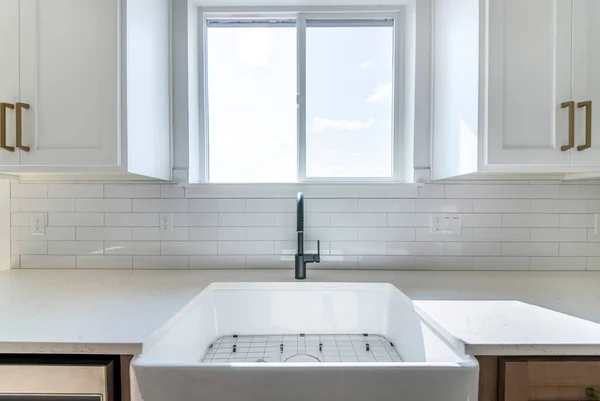 Weißes Porzellanspüle mit schwarzem Wasserhahn in einer Küche gegen das Fenster — Stockfoto