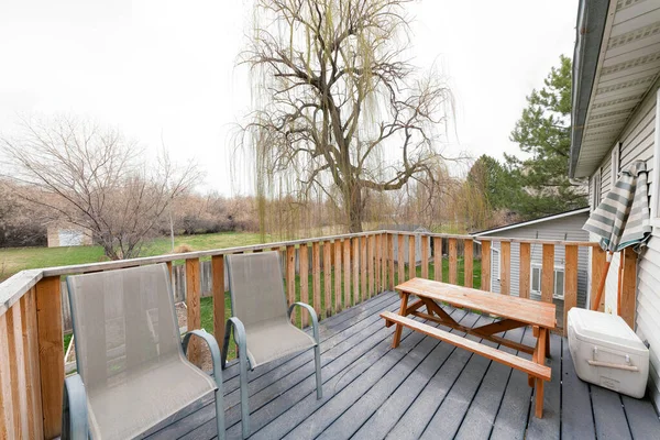 Deck de uma casa com poltronas cinzentas, mesa de jantar ao ar livre com banco, recipiente mais frio e guarda-chuva — Fotografia de Stock