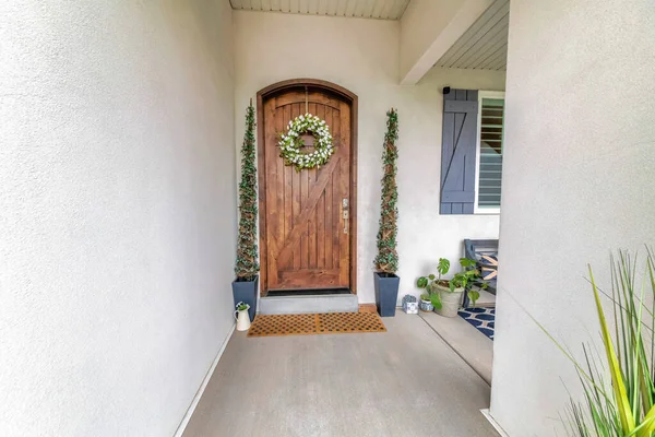 Arched wooden door with digital entry access, wreath and topiary spiral shrubs