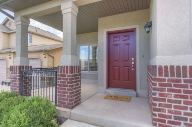 Verandasında kırmızı tuğlalar ve parmaklıklar olan bir evin kırmızı ön kapısı.