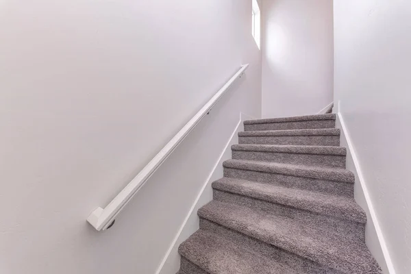 Carpeted stairs with wall-mounted white handrailing upstairs