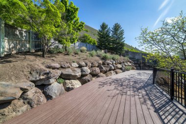 Tepedeki tahta güvertede demir parmaklıklar ve dağ yamacının manzarası var.