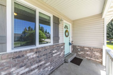 Nane yeşili ön kapısı, çelengi, cam paneli ve iki kilitli kutusu olan bir evin verandası.