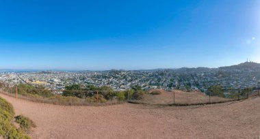 Tepedeki toprak zeminde tel örgüler ve körfez yerleşim alanı manzarası var.