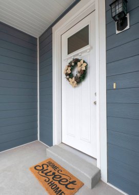 Pencere panelinin altında çelenk olan bir evin dikey beyaz ön kapısı