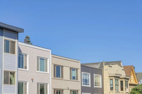 Neighborhood in San Francisco, California with box roofs exterior against the clear blue sky. Complex houses with box roofs from the left and two houses with gable roofs on the right.