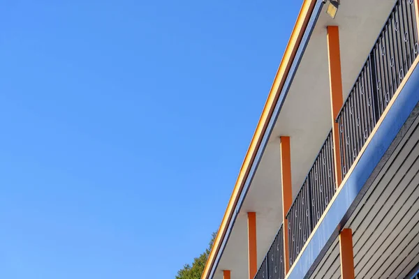 San Francisco, CA 'da açık mavi gökyüzüne karşı terası olan bir binanın alçak açılı görüntüsü. Sağda turuncu sütunları ve siyah işlemeli demir parmaklıkları olan bir bina var..