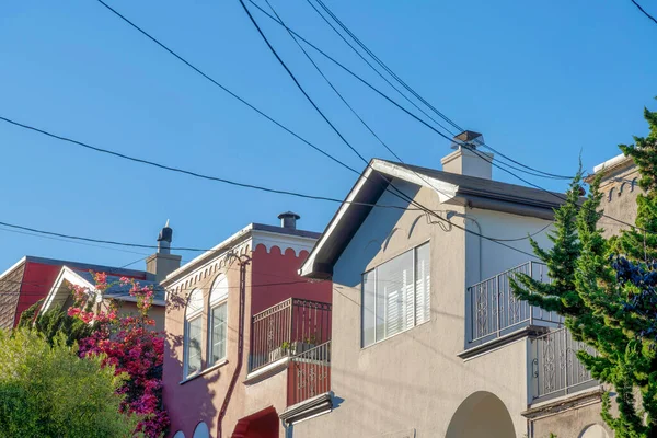 San Francisco, California 'daki kompleks evler. Balkonları ve solunda ağaçlar olan bir mahalle ve açık mavi gökyüzüne karşı elektrik kabloları..