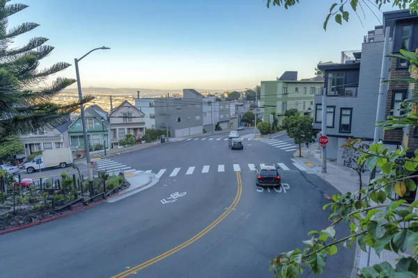 High angle view of road intersection with vehicles passing at San Francisco, California. Intersection road with pedestrian lanes near the residences and a view of skyline at the background.