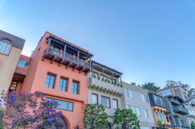 San Francisco, California 'da balkonlu evlerin alçak açılı görüntüsü açık gökyüzüne karşıdır. Ön tarafında ağaçlar olan bir mahalle ve dış tarafında resim pencereleri olan bir mahalle..