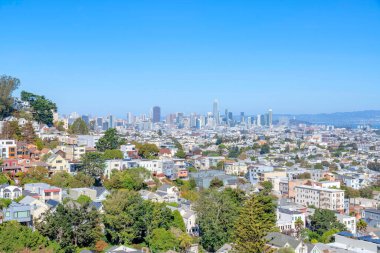 San Francisco, Kaliforniya 'da yerleşim ve ticari binalar manzaralı bir şehir manzarası. Önde ağaçlar ve arkada açık mavi gökyüzüne bakan gökdelenler var..