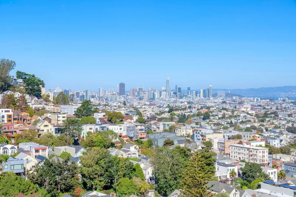 San Francisco, Kaliforniya 'da yerleşim ve ticari binalar manzaralı bir şehir manzarası. Önde ağaçlar ve arkada açık mavi gökyüzüne bakan gökdelenler var..