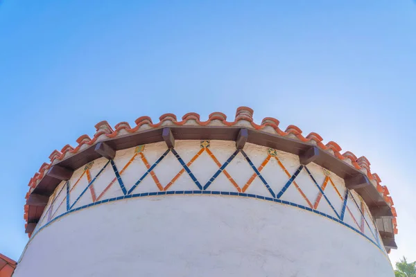 Low angle view of a curved wall with orange and blue trims in San Francisco, California. Mediterranean style building with concrete tile roof against the clear blue sky background.