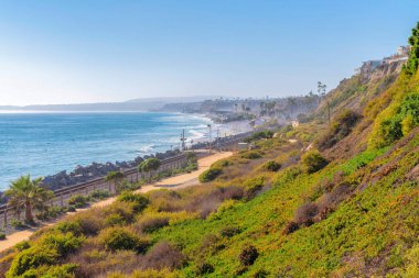 San Clemente, California 'daki bir dağ yamacının tepesinden sahili ve tren raylarını görüyorum. Sahil bölgesinin yüksek açılı görünümü açık gökyüzü arkaplanını tarıyor.