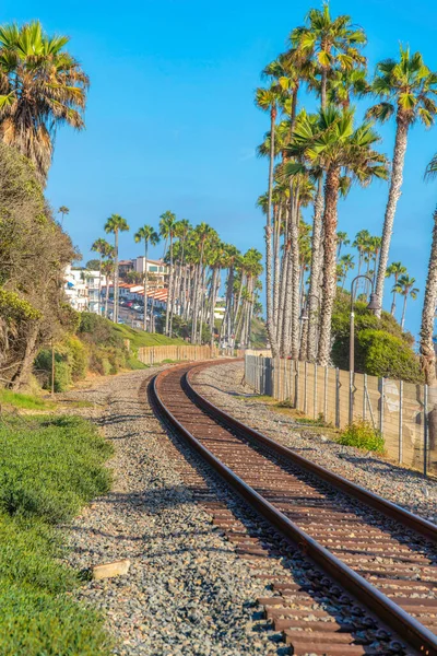 Kaliforniya, San Clemente 'de taşlı tren rayları. Sağdaki tel çitin yanındaki demiryolu ve arka planda binalar ve palmiye ağaçları görünüyor..