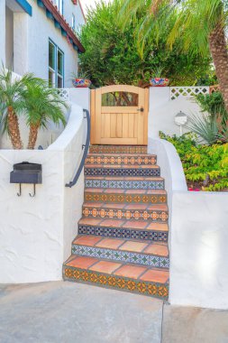 Ön kapının merdivenlerinde fayans merdivenleri ve San Clemente, CA 'deki süslü fayans merdivenleri var. Beyaz bir duvarın ortasında merdivenler, korkuluklar ve evin içindeki ağaçlara karşı bir kapı..