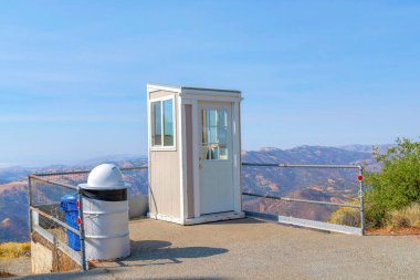 San Jose, California 'daki Gözlemevi' nin açık hava bilet gişesi. Bilet gişesi metal parmaklıkların yanında sağda çöp bidonları ve arkadaki dağ ve gökyüzü manzarasına karşı..