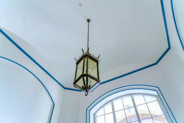 Single lamp chandelier in a low angle view at San Jose, California. Chandelier against the view of the ceiling and arched window with blue trims and frames.
