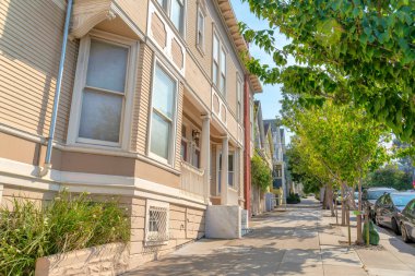 San Francisco, California 'daki yerleşim yerlerinin önünde beton levhalar var. Ağaçlar ve araçlar arasında soldaki bej evden başlayan bir sıra ev var..