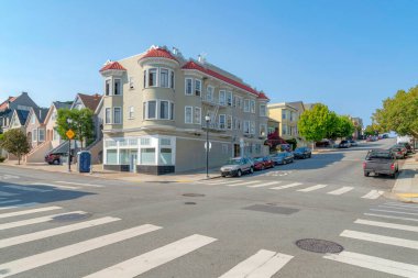 San Francisco, California 'daki kavşak yolu boyunca yerleşim yerleri. Köşede bir apartman var. Yolun kenarında yaya geçitleri olan araçlar var..