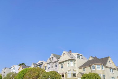 San Francisco, California 'da çatısı olan evleri alçak açılı görüyor. İki katlı evlerin önünde açık mavi gökyüzü arka planına karşı ağaçlar var..