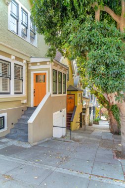 San Francisco, California 'da yokuş aşağı giden evler. Garajın solunda yüksek ön kapılı evler var. Sağdaki ağaçların yanındaki beton kaldırımın yanında..