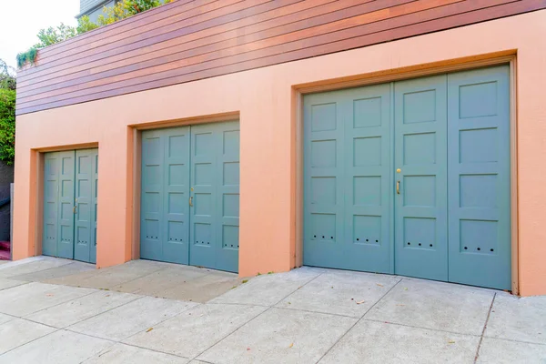 Three side-hinged garage doors with gold door handles at San Francisco, California. Garage exterior below the wooden fence with plants above.