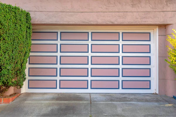 Garage door with white grid trims and pink panels with blue frames at San Francisco, California. Garage exterior with sectional door and concrete driveway with topiary shrubs on the side.