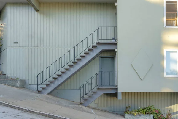 カリフォルニア州サンフランシスコの2階建てのアパート 緑豊かな灰色の壁に対して鉄の手すりと傾斜舗装の近くに2つの階段の入り口があります — ストック写真